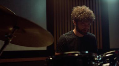 Neşeli sanatçı salonda dinleniyor. Gülümseyen davulcu stüdyoda kameraya bakıyor..