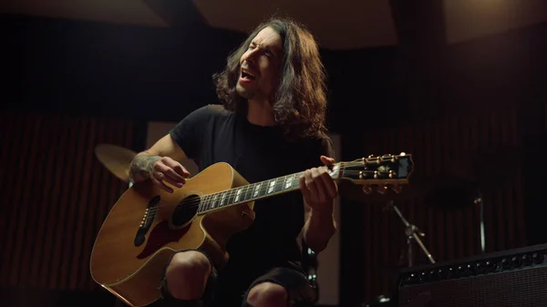 Hombre excitado tocando la guitarra en el estudio de música. Chico alegre cantando en el hall oscuro. — Foto de Stock