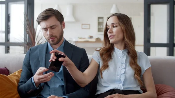 En sint kvinne tar med seg mannetelefonen hjem. Kjedelig par som sitter på sofaen. – stockfoto