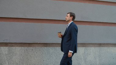 Yandan bakan adam kahve içiyor. Adam dışarıda kahveyle çalışacak.