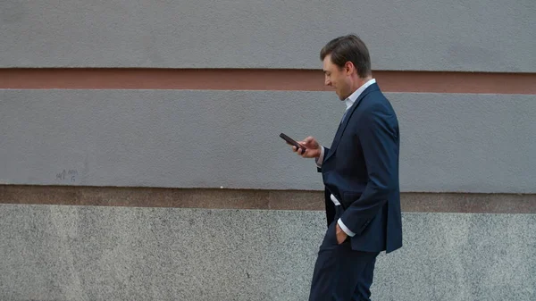 Πλευρικός επιχειρηματίας που περπατάει με το τηλέφωνο. Άνθρωπος που ψάχνει σε εξωτερικούς χώρους smartphone — Φωτογραφία Αρχείου