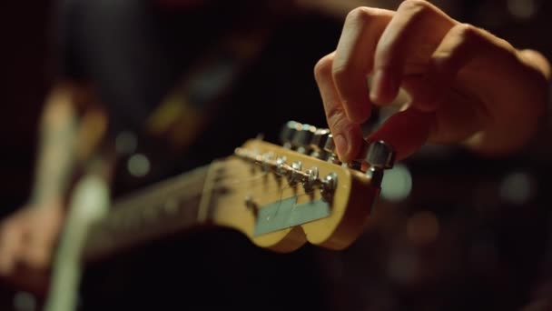 Gitarist draaiknoppen op fretboard in studio. Man met gitaar in hal. — Stockvideo