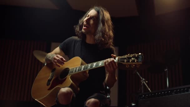 Aufgeregter Mann spielt Gitarre im Musikstudio. Fröhlicher Kerl singt in dunkler Halle. — Stockvideo