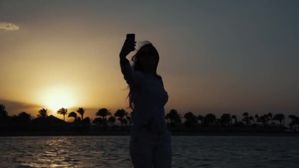 在日落海岸用手机自拍的迷人女人. — 图库视频影像