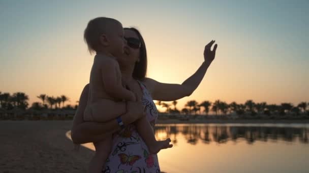 Bela jovem mãe segurando pequena criança a mãos na praia do pôr do sol. — Vídeo de Stock