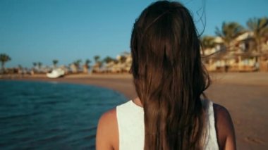 Denizde yürüyen rahat bir kadın. Güzel kız tatilini güneşli sahil şeridinde geçiriyor.