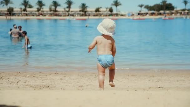 Mały chłopiec cieszący się ciepłą wodą nad morzem. Cute dziecko działa na plaży piasku. — Wideo stockowe