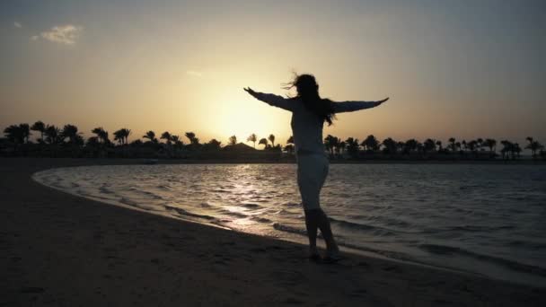 젊은 여자가 모래사장에서 춤을 추고 있어요. 아름다운 소녀가 해 가는 바다 근처에서 즐거운 시간을 보낸다. — 비디오