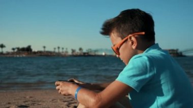 Deniz koyunda cep telefonuyla oturan mavi tişörtlü yakışıklı genç adam..