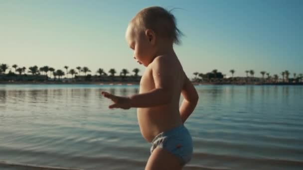 Adorable niño lindo caminando a lo largo de la costa. Chico feliz salpicando agua en la playa. — Vídeo de stock