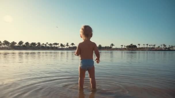 Активный мальчик брызгает водой на море. Маленький ребенок гуляет на летнем пляже. — стоковое видео