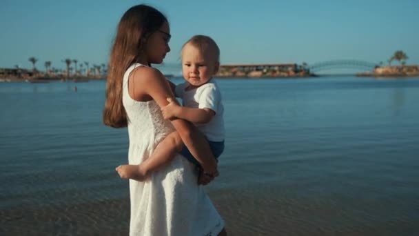 長いです毛ティーン女の子歩くとともに日当たりの良い海辺とともに赤ちゃん男の子オン手. — ストック動画