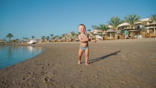 Gioioso bambino che cammina lungo la costa di sabbia all'acqua durante la giornata estiva. — Video Stock