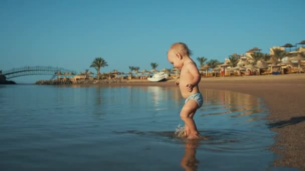 여름 방학 때 모래 해변에서 따뜻 한 바다에서 물을 튀기는 사랑 스러운 아기. — 비디오