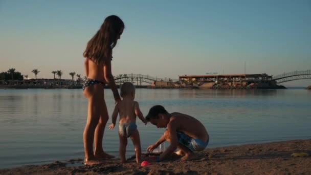 Adolescentes felices divirtiéndose con lindo bebé en la playa de arena en el balneario. — Vídeos de Stock