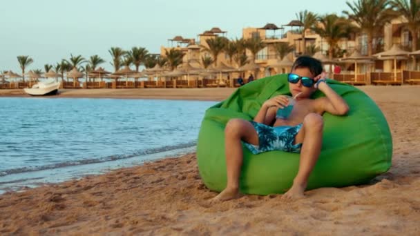 Um adolescente que gosta de limonada na costa. Bonito jovem sentado à beira-mar. — Vídeo de Stock