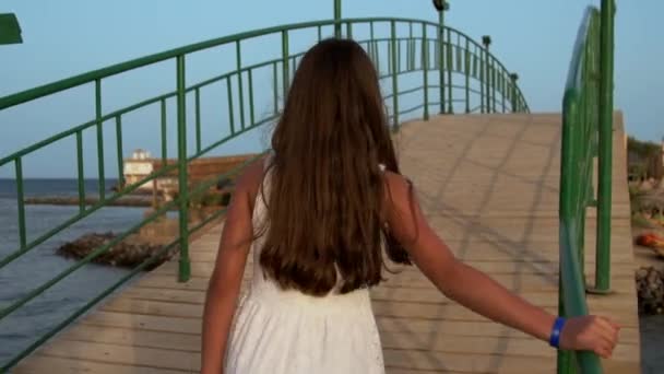 Fiatal nő fehér ruhában átsétál a hídon napkeltekor.. — Stock videók