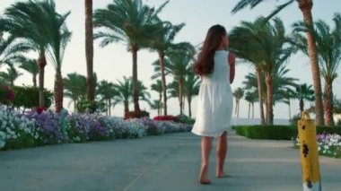 Palmiye ağaçlarının arasında dinlenen güzel bir kız. Bahçede yürüyen genç bir kadın.