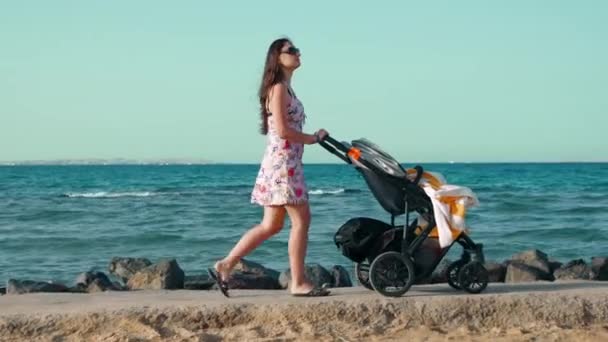 Lang haar jonge vrouw wandelen langs de promenade met kinderwagen in de zomer vakantie. — Stockvideo