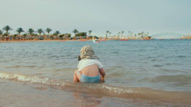 Tatil köyünde suda yürüyen tatlı bir çocuk. Bebek sahil şeridinde oynuyor..