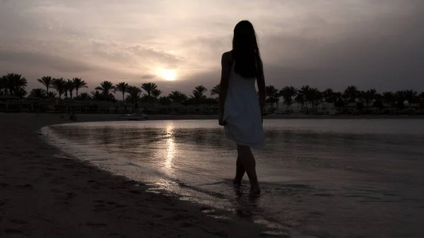 Ξυπόλητη γυναίκα που περνάει το ηλιοβασίλεμα στην παραλία. Όμορφο κορίτσι περπατά στην ακτή. — Φωτογραφία Αρχείου