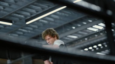 Genç kickboksçu spor salonunda tekme atıyor. Sporcu ringde dövüşmeye hazırlanıyor.