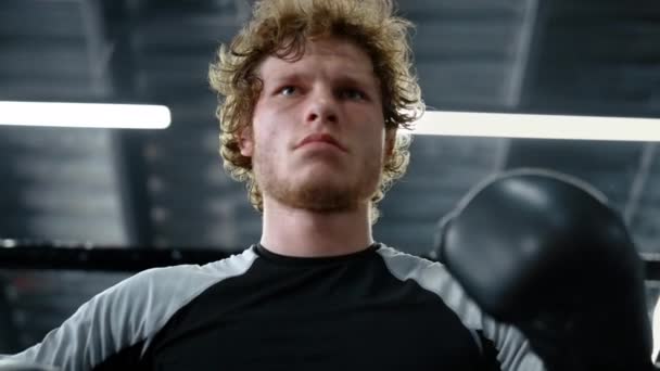 Θυμωμένος πυγμάχος κοιτάζει την κάμερα στο γυμναστήριο. Αθλητής που ελέγχει γάντια πυγμαχίας — Αρχείο Βίντεο