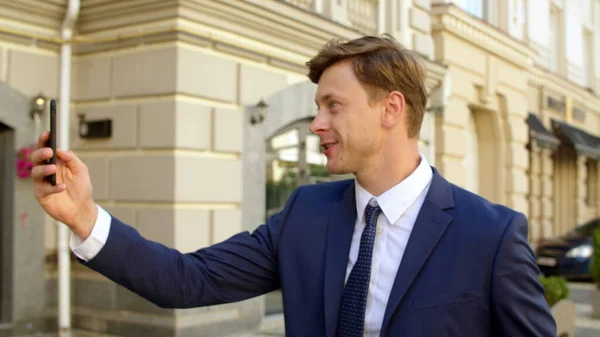 Emotional business man waving hand at video chat on mobile phone outdoors