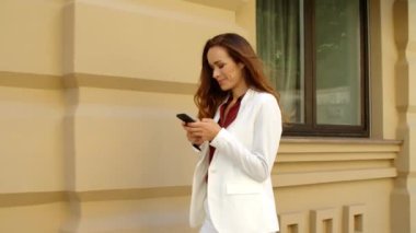 Mutlu iş kadını dışarıda cep telefonuna mesaj atıyor. Gülümseyen iş kadını