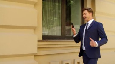 Kızgın iş adamı dışarıda cep telefonundan konuşuyor. Endişeli iş adamı yürüyor