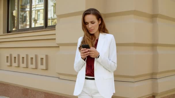 Pensando mujer de negocios mensaje de texto en el teléfono móvil al aire libre — Vídeos de Stock