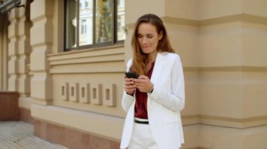 Dışarıda cep telefonuyla mesajlaşan şakacı bir iş kadını. Gülümseyen kadın