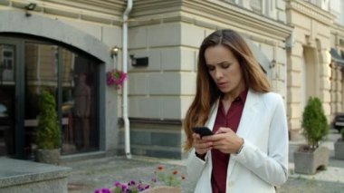 Odaklanmış iş kadını dışarıda cep telefonuna mesaj yazıyor.