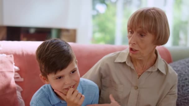 Nachdenklicher Enkel sitzt mit Großmutter auf Sofa. Junge hält Hand am Kinn — Stockvideo