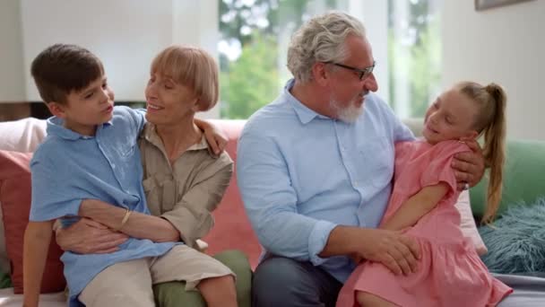 Szczęśliwy dziadek i babcia siedzi na kanapie z wnukami na kolanach — Wideo stockowe