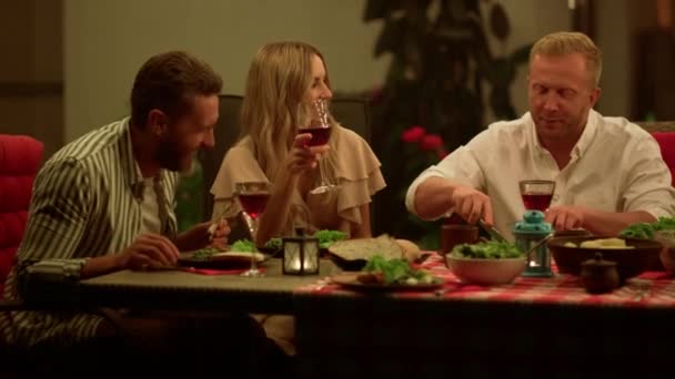 Друзі їдять їжу під час вечері. Чоловіки і жінка розмовляють за обіднім столом — стокове відео