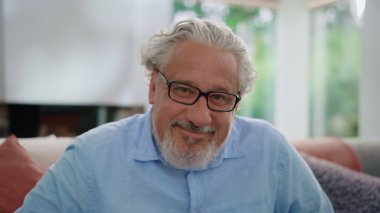 Kıdemli adam kameraya gülümsüyor. Odadaki kanepede oturan olgun bir adamın portresi.