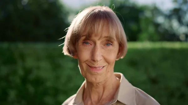 Femme âgée souriante regardant avec une caméra. Femme mûre debout dans un parc vert — Photo