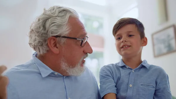 Nonno che parla nipote in camera. Allegro ragazzo seduto sulle ginocchia dei nonni — Foto Stock