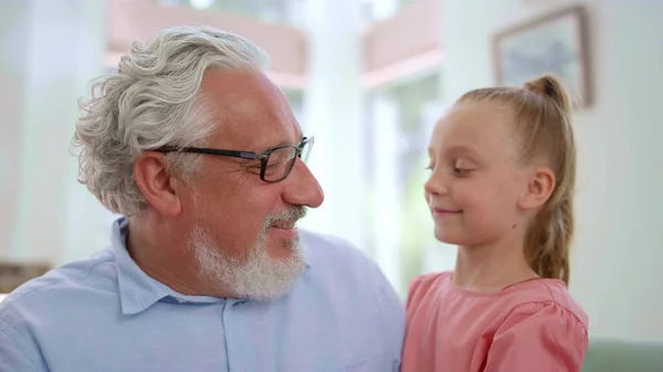Nonno sorridente che guarda la nipote. Ragazza abbracciare l'uomo anziano in camera — Foto Stock