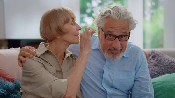 Seniorkvinne som tar av briller fra en mann. Modent par som sitter på sofaen – stockfoto