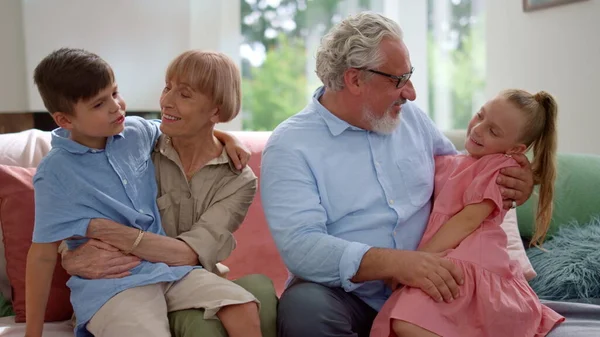 Buon nonno e nonna seduti sul divano con nipoti in grembo — Foto Stock
