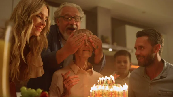 Familia celebrando cumpleaños abuela en la cocina. Mujer mirando pastel —  Fotos de Stock