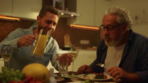 아버지와 성인 아들이 식탁에서 식사를 한다. 유리에 주스를 붓는 사람 — 비디오