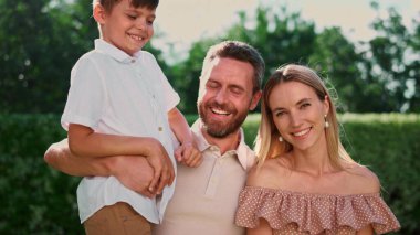 Mutlu anne ve baba ve oğul kameraya gülümsüyor. Neşeli bir adam çocuğu elinde tutuyor