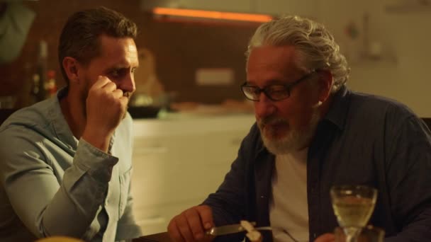 Älterer Vater und erwachsener Sohn sitzen am Tisch. Ernste Männer unterhalten sich beim Abendessen — Stockvideo