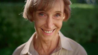 Olgun bir kadın kameraya bakıyor. Yeşil parkta gülümseyen yaşlı bayan.