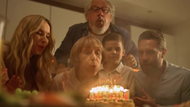 La familia felicitando a la abuela por el cumpleaños. Mujer soplando velas en el pastel — Vídeo de stock