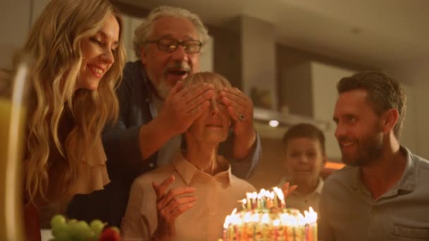 Família que celebra aniversário de avó na cozinha. Mulher olhando para bolo — Vídeo de Stock