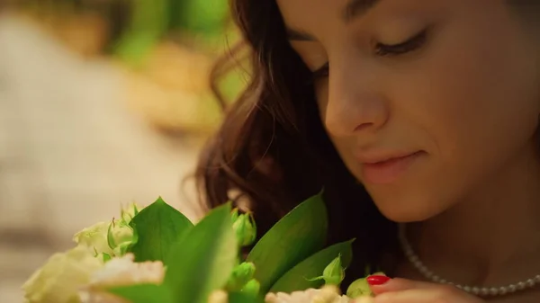 Kaunis morsian ihailee kukkia puutarhassa. Nainen koskettaa kukka terälehtiä puistossa — kuvapankkivalokuva